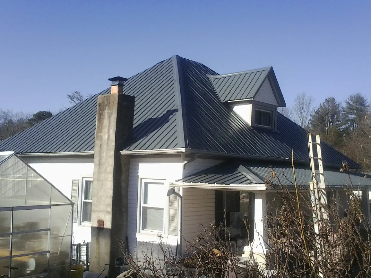 Dark blue standing seam metal roof on a white farmhouse with dormer — Slate & Tile Roof Repair by Roofing Brothers in Gresham