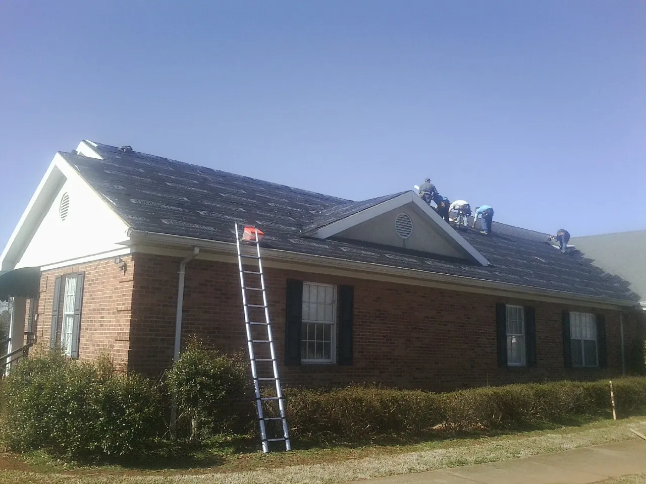 Crew tearing shingles off a brick ranch roof with a ladder set — Emergency Roof Repair work by our crew in Gresham