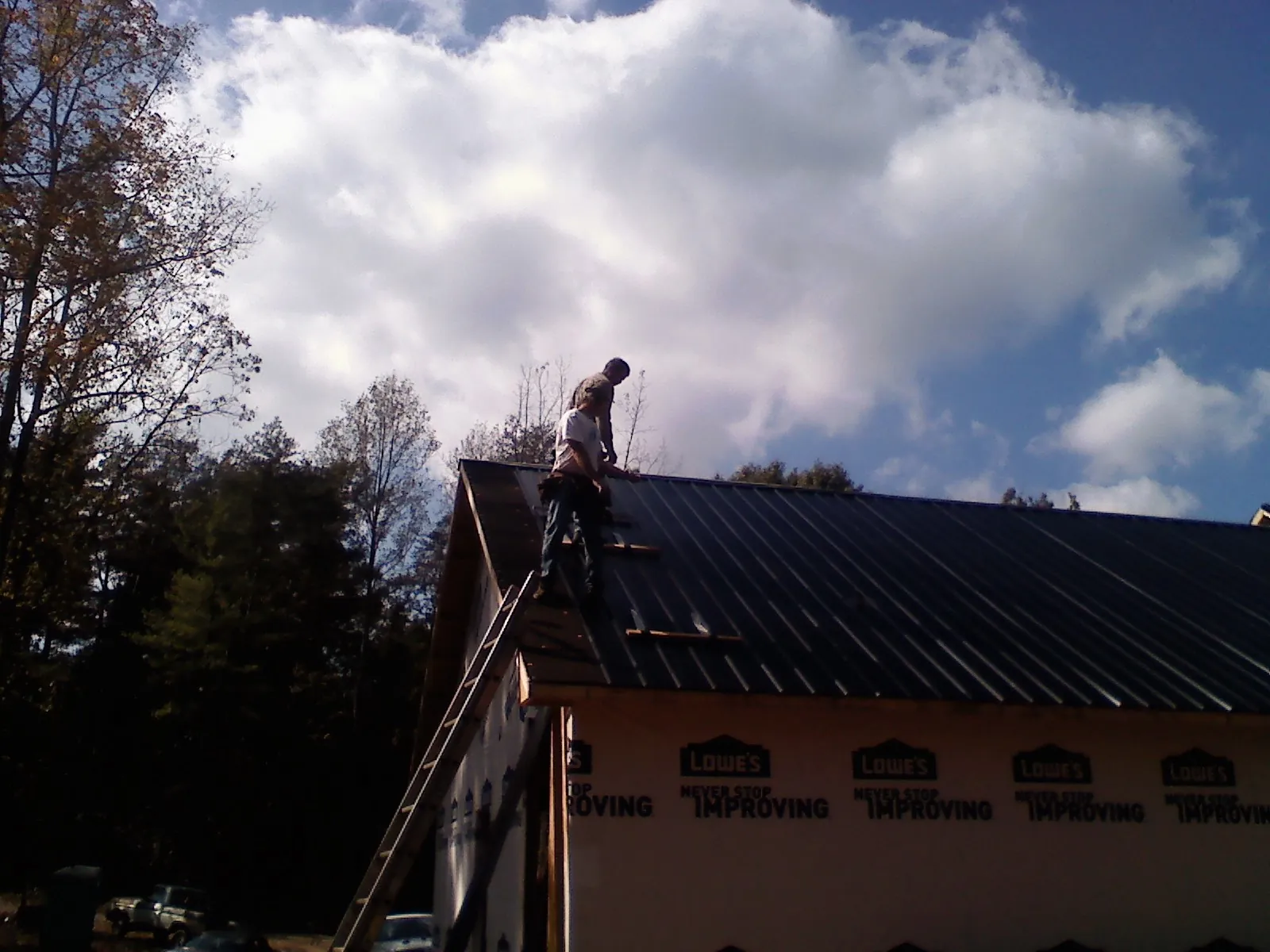 Roofer fastening dark metal panels high against a cloudy sky, from a Roof Inspection job in Gresham