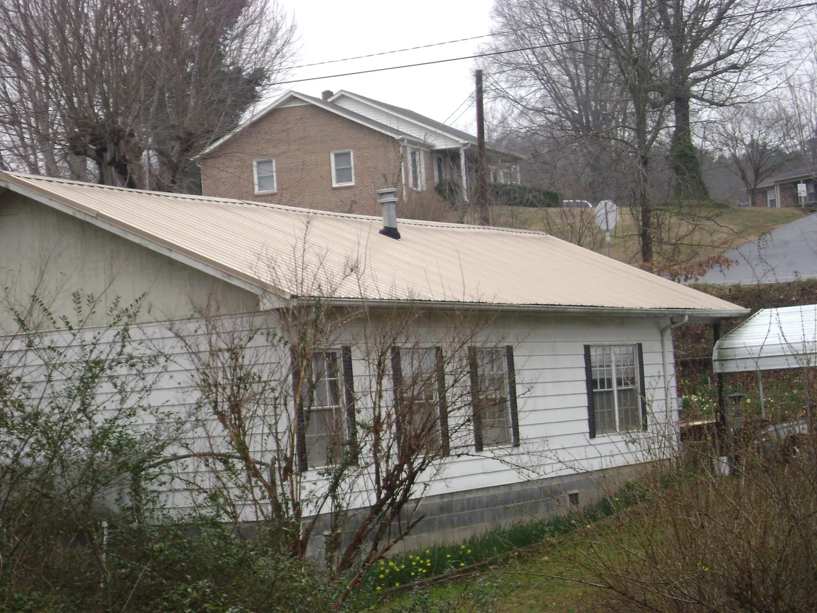 Tan metal roof on a white sided house set into a hillside — Commercial Roofing by Roofing Brothers in Gresham